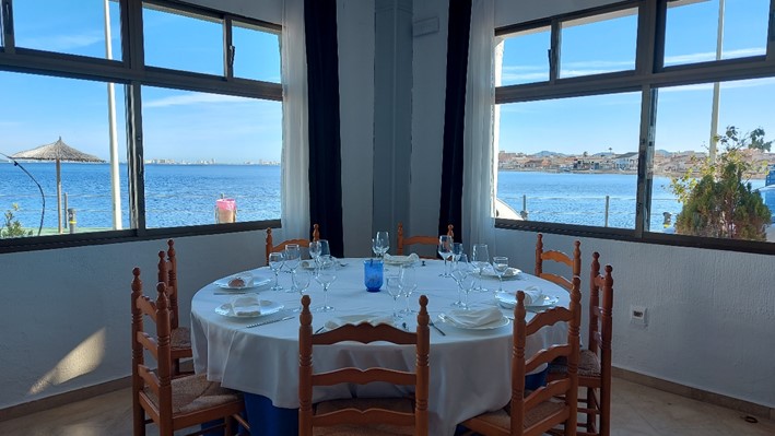 Interior del restaurante del club náutico Los Nietos. Se ve una mesa y dos ventanas con vistas a la Manga del Mar Menor