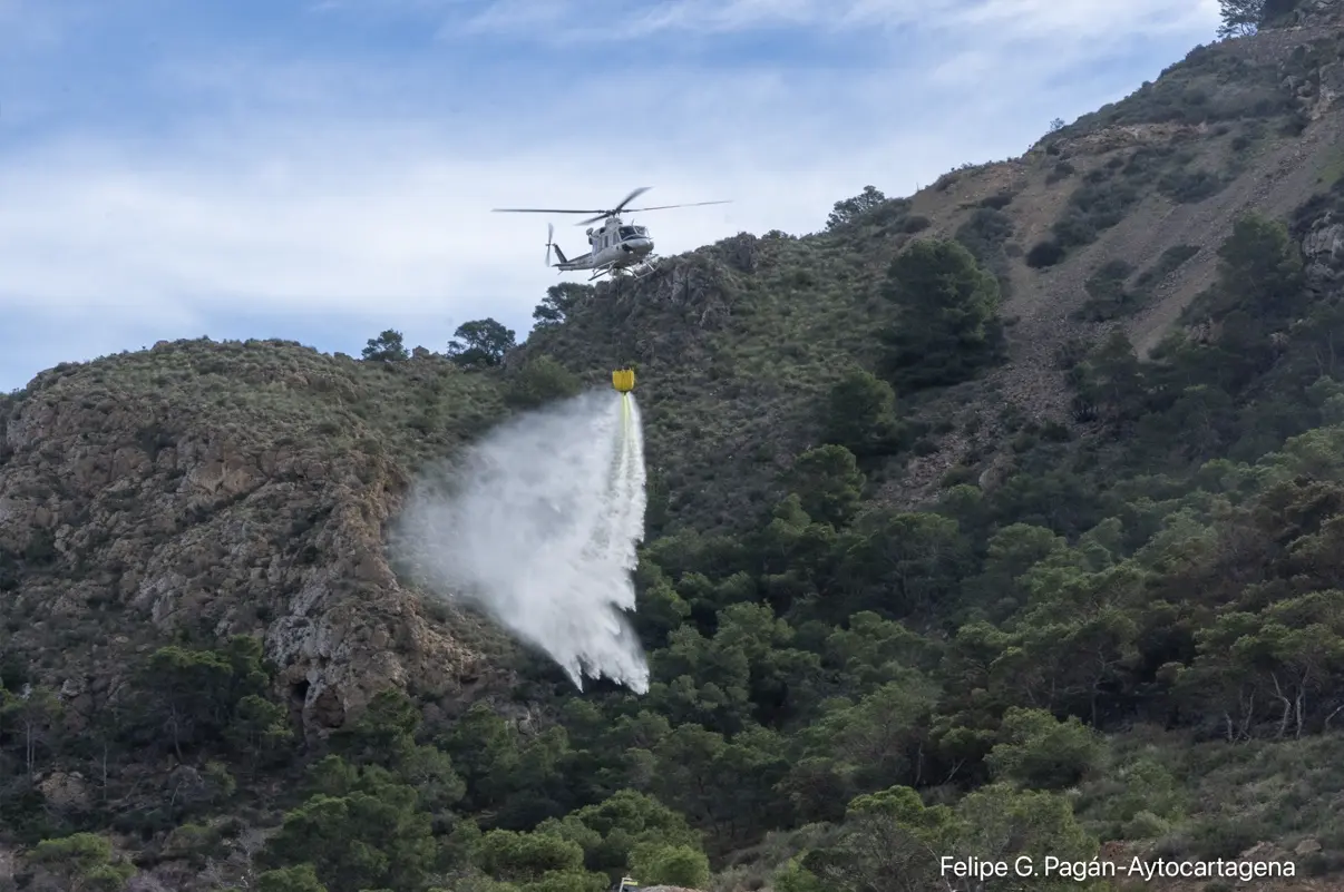 Helicóptero de extinción descargando agua sobre una ladera montañosa en Cabo Tiñoso, durante las labores para estabilizar el incendio forestal.