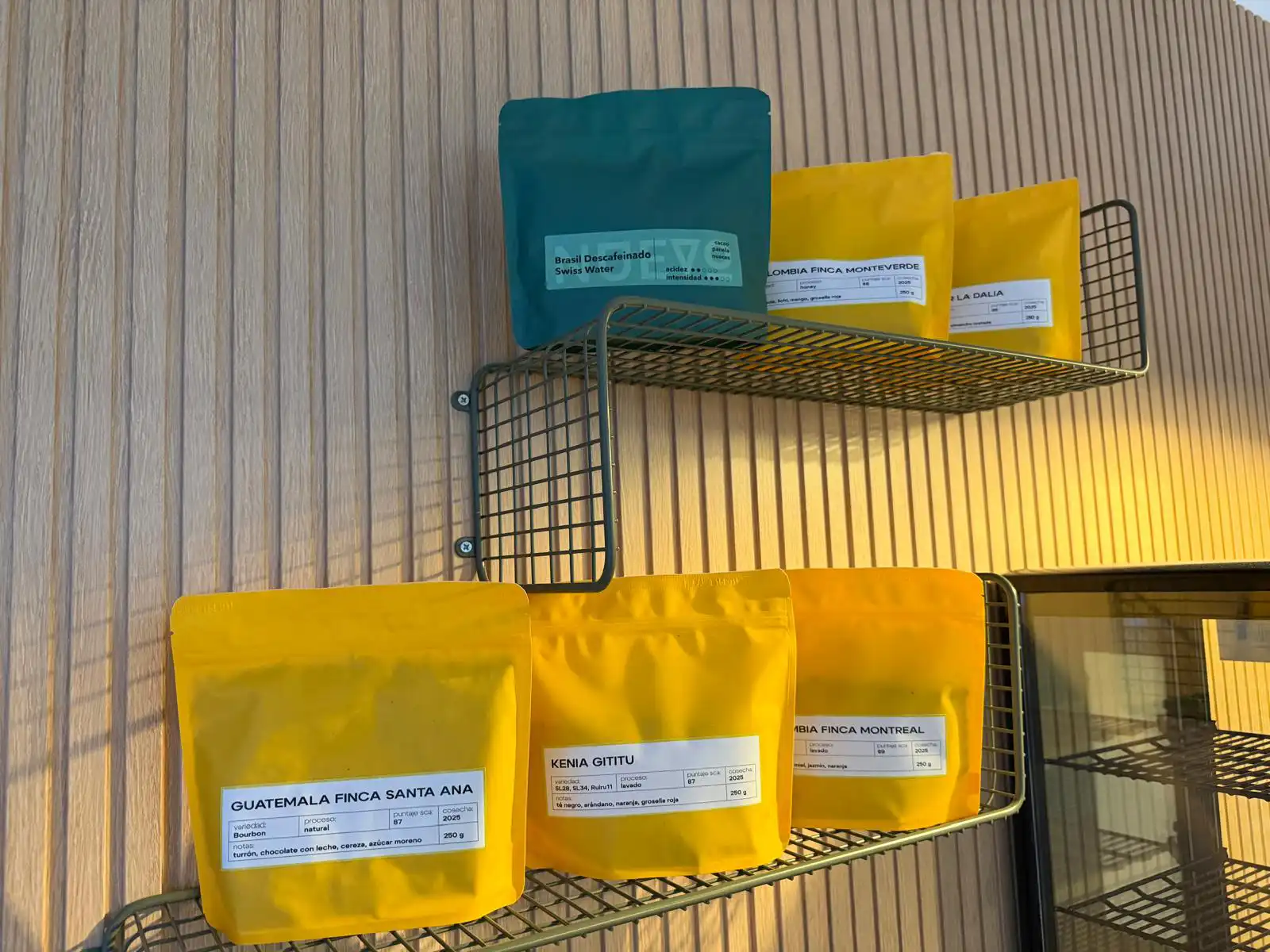 Bolsas de café de especialidad de distintos orígenes como Guatemala, Kenia, Colombia y Brasil expuestas en estanterías metálicas en el interior de Café Verde.