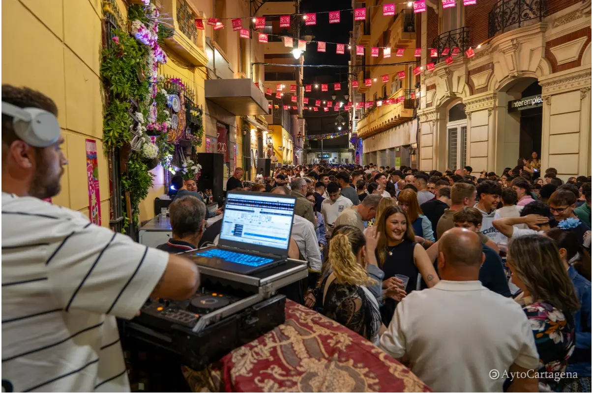 Calle del centro de Cartagena abarrotada durante las Cruces de Mayo con DJ animando y decoración festiva nocturna