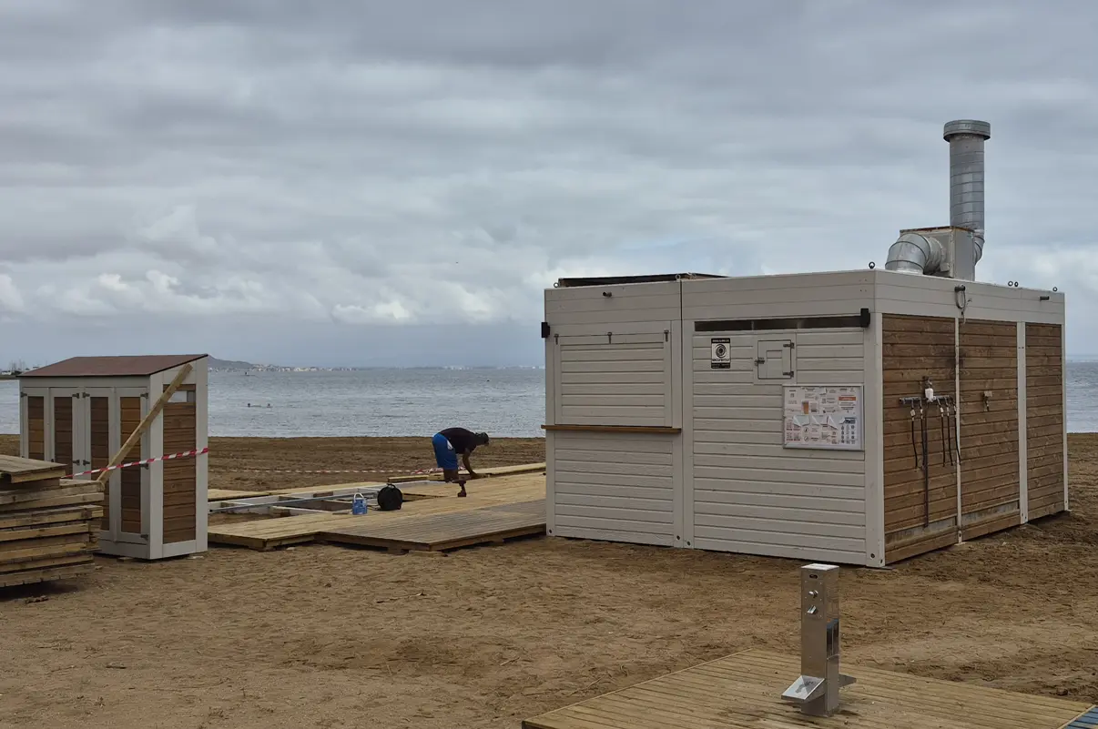 rabajos de instalación del chiringuito de La Cangreja en la playa de Poniente de Islas Menores, con operarios ultimando la estructura de madera frente a las aguas del Mar Menor.